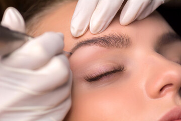 Obraz na płótnie Canvas Permanent eyebrow makeup. Cosmetologist applying tattooing of eyebrows.