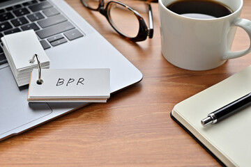 On a desk with a laptop, glasses, coffee, and a notebook, a vocabulary book was placed open There. The word BPR is there. It's an acronym that means Business Process Re-engineering.