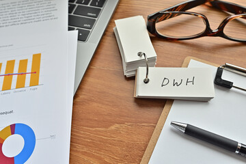 There is a piece of paper with a graph printed on it, a clipboard, and an open vocabulary book on the desk. The word DWH is there. It's an acronym that means Data WareHouse.