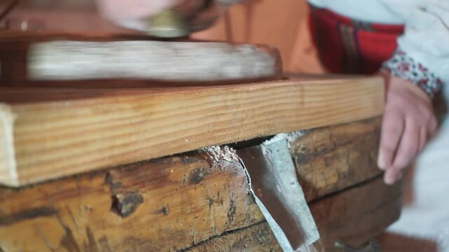 The ancient Quern stone hand mill with grain. The man grinds the grain into flour with the help of a millstone. Men's hands on a millstone. Old grinding stones turned by hands
