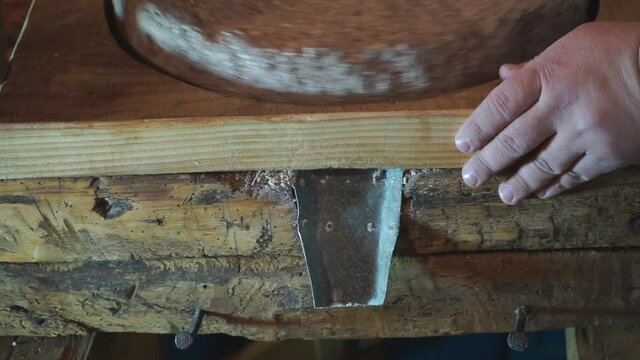 The ancient Quern stone hand mill with grain. The man grinds the grain into flour with the help of a millstone. Men's hands on a millstone. Old grinding stones turned by hands