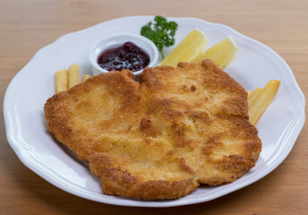 Crumbed pork escalope called Schnitzel served with French fries, cranberry sauce and lemon