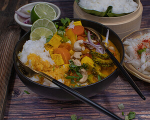 Thai vegan mixed vegetables red curry and rice on wooden table in black bowl, close up