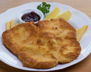 Crumbed pork escalope called Schnitzel served with French fries, cranberry sauce and lemon