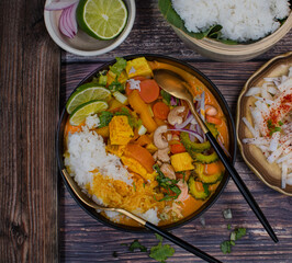 Thai vegan mixed vegetables red curry and rice on wooden table in black bowl, top view