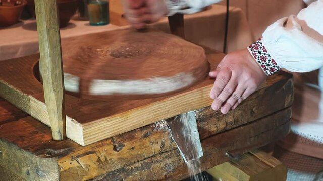 The ancient Quern stone hand mill with grain. The man grinds the grain into flour with the help of a millstone. Men's hands on a millstone. Old grinding stones turned by hands