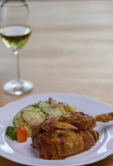 Grilled half chicken served with a German potato cucumber salad with bacon and a glass of wine in the back