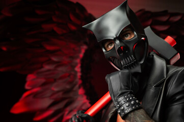 a man in a demon skull mask in a leather cloak with an axe on a background of black and red wings