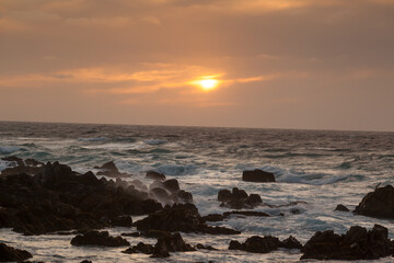 Obraz premium Ocean crashing onto a rocky shore at sunset