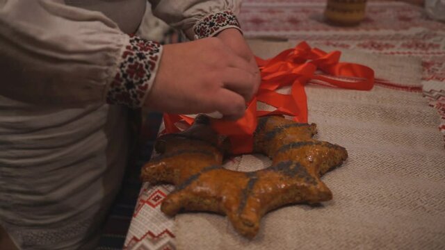 A man baker puts a gingerbread on the table tying it with a red ribbon to perform an ancient rite