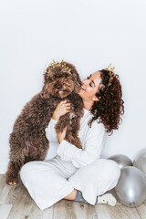 Beautiful brunette woman in pajamas hugging her dog and looking at it in the New Year's party at home. They are wearing Christmas headbands. New Year's Eve party at home concept