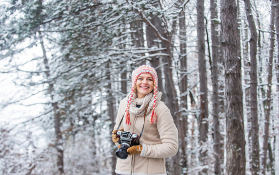 Photographer photographing on snowy winter day. happy woman warm clothes fashion. winter travel vacation. stylish hipster traveler. woman holding photo camera. taking picture in winter forest