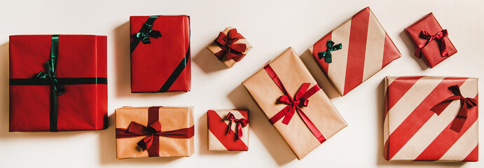 Flat-lay of festive craft gift boxes in wrapping paper decorated with ribbons and green and red bows over plain white background, top view. Christmas boxing day concept