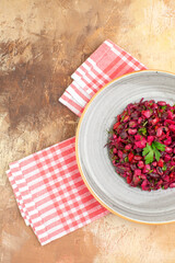 side view of plate of a red salad on the right-hand side with greens on it with checked napkin at the side on a wooden backgorund