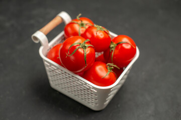 Close up view of collection of fresh tomatoes in a white basket on dark background
