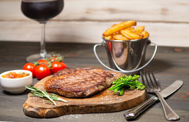grilled rib eye steak with handmade chips, cherry tomatos and broccoli on a dark wooden table 