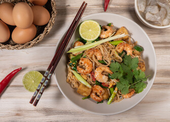 pad thai noodles with tofu and prawns in a white plate on a old white wooden table