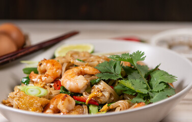 pad thai noodles with tofu and prawns in a white plate on a old white wooden table