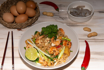 pad thai noodles with tofu and prawns in a white plate on a old white wooden table