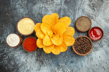 Above view of potato chips with different spices mayonnaise and ketchup on gray background