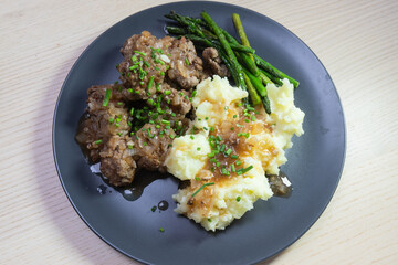A plate of meatball steak with asparagus and mashed potato.