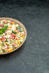 side view of bowl of vegetable salad on the left side with green on it on dark green background