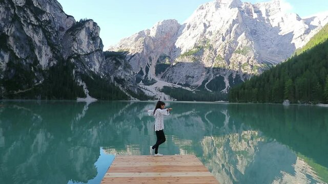 Girl balancing on a dock at lake Lago di Braies, sunny day, in Dolomites, Italy - Slow motion