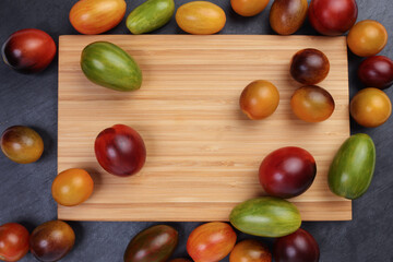 Red orange yellow green tomato mix variety on around wooden chopping board frame copy text space over black slate stone background