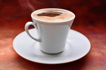 Full to the brim white coffee cup on white porcelain saucer strong black invigorating coffee with foam and thick aromatic smoke on brown background