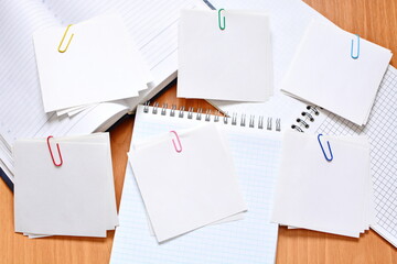 Several pieces of white blank sheets of note paper in groups held together with paper clips on notebooks and daily planner. Copy space