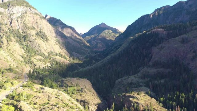Aerial Drone Lowering Motion of Beautiful Ouray Colorado Mountain Range and Cars Driving on Highway 550 Surrounded by Thick Pine Tree Forest and Power Lines in the Rocky Mountains