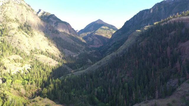 Aerial Drone Reveal of Beautiful Ouray Colorado Mountain Range and Cars Driving on Highway 550 Surrounded by Thick Pine Tree Forest and Power Lines in the Rocky Mountains