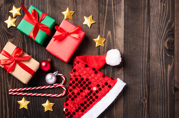 Christmas decor composition present. Flat lay top view of Santa hat, star, ornament and Christmas gift box decorations on black wooden background with copy space, New year card concept