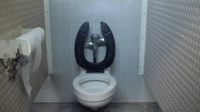 A public toilet with the seat up in a park bathroom and toilet paper blowing in the wind