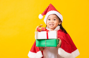 Asian little cute girl smile and excited, Kid dressed in red Santa Claus hat hold gift box on hands concept of holiday Christmas Xmas day or Happy new year, studio shot isolated on yellow background