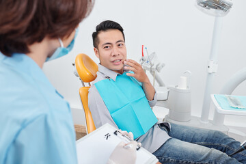 Vietnamese man sitting in dental chair and complaining about toothache