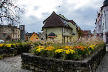 Cesis, Latvia - Rauna Gate, flower beds with yellow and orange flowers on a historic site, houses in the old town, gray clouds in the sky, in the fall during the day.