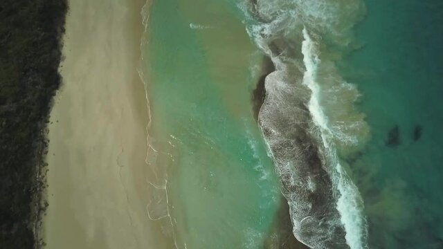 Aerial view of ocean waves crashing onto a big empty beach in Western Australia.
