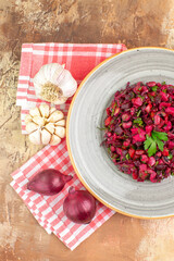 top close view of bowl of a red salad with greens on it on a wooden backgorund with vegetables at the side with checked napkin