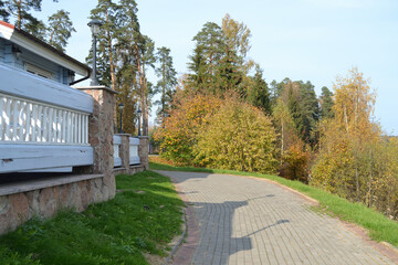 A winding path going deep into the forest with tall trees and young pines, near a beautiful stone fence.  Rest in a country park. Demino / Rybinsk, Russia - October 3, 2020.