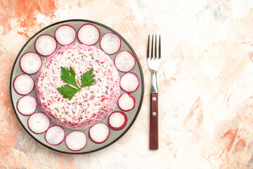 Above view of delicious chicken salad with beet served with chopped red radishes on a gray plate and fork on mixed color background