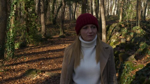 Woman in red hat and white turtleneck sweater walks in autumn forest, Dolly Out