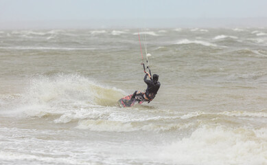 A kiteboarder riding on the waves in the sea on a rainy day.