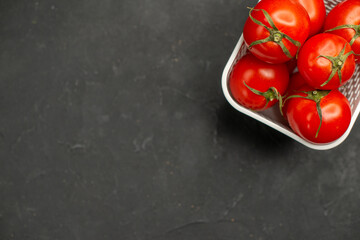Half shot of collection of fresh tomatoes in a white basket on the left side on dark background