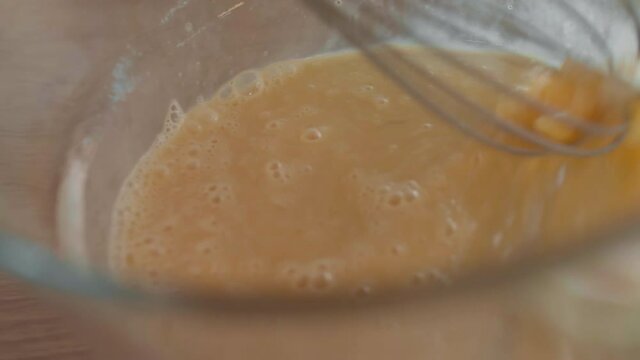 Close-up of raw eggs getting mixed by whisk in large glass bowl by unrecognizable person