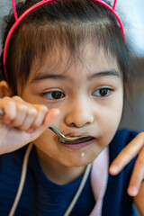 Female asian child while eating rice using spoon. Child enjoys eating rice by her own. Child learning to use spoon and eat by her own