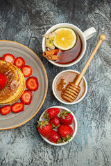 top view yummy pancakes with strawberries and cup of tea on light desk fruit cake sweet