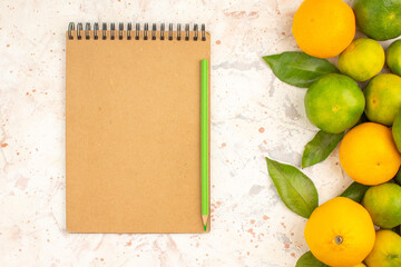 Horizontal view of fresh tangerines on the left side and notebook with pen on mixed color background