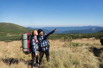 couple in love tourists man and woman stand on a mountain plain Pointing with one hand to the empty space for the text. Hiking concept.