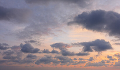 A beautiful evening sky full screen. Purple cumulus clouds on a gentle blue background. Backlit by the sun in shades of pink and orange.